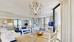 A modern hotel room with a dining area, a living room, and a large window with curtains. - Two Gulf-view condos in one - balconies, pool, hot tubs, gym & beach access (Miramar Beach)