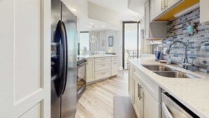 A modern kitchen with a stainless steel refrigerator, a double sink, and a backsplash of blue and gray tiles. - Two Gulf-view condos in one - balconies, pool, hot tubs, gym & beach access (Miramar Beach)