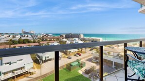 A balcony with a view of a coastal town, including buildings and a beach. - Two Gulf-view condos in one - balconies, pool, hot tubs, gym & beach access (Miramar Beach)