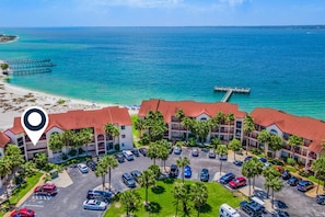 A hotel with a parking lot, multiple floors, and a view of the ocean. - Condo with private balcony, pool, grills, central AC, & W/D (Navarre Beach)