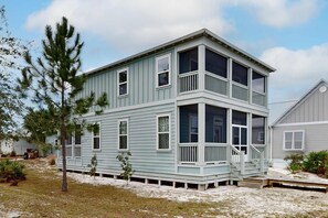 A two-story house with a balcony on the second floor, surrounded by a sandy landscape and sparse vegetation. - Lovely Home w/ Screened-In Porches, Balcony & Shared Pool - Walk to the Beach (Port St. Joe)
