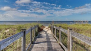Een houten looppad dat naar een strand leidt, onder een heldere hemel.