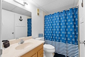 A bathroom with a sink, mirror, and a blue curtain with anchor patterns. - Beachfront 2BR Condo w/ Pool & Balcony Views (Panama City Beach)