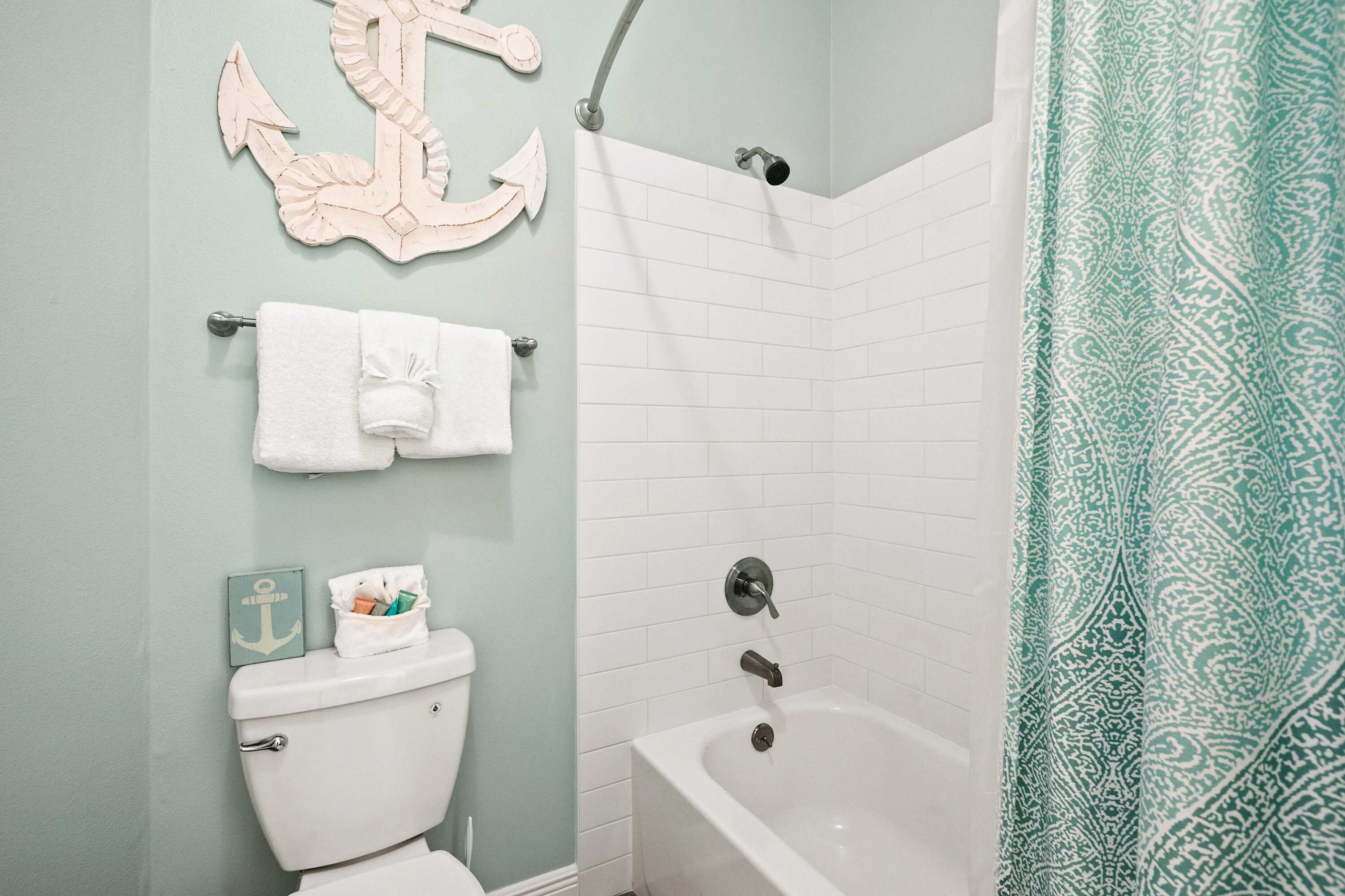 Ein Badezimmer mit einer weißen Badewanne, einer Dusche und einem WC. Ein Handtuchhalter mit Handtüchern und ein dekorativer Anker sind an der Wand angebracht.