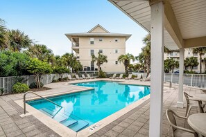 A swimming pool with a 3 FT depth marker, surrounded by lounge chairs and palm trees, with a building in the background. - Lovely condo with shared pool, washer&dryer, high-speed WiFi, and central AC (Navarre Beach)