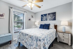 A bedroom with a bed, two bedside lamps, a nightstand, a bench, and a ceiling fan. - Lovely condo with shared pool, washer&dryer, high-speed WiFi, and central AC (Navarre Beach)
