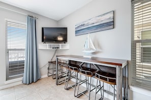 A modern living room with a flat-screen TV, a sailboat decoration, and a bar area with stools. - Lovely condo with shared pool, washer&dryer, high-speed WiFi, and central AC (Navarre Beach)