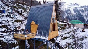 A wooden cabin with a sloped roof, a small balcony, and a wooden staircase. - Awe Glamping (Manali)