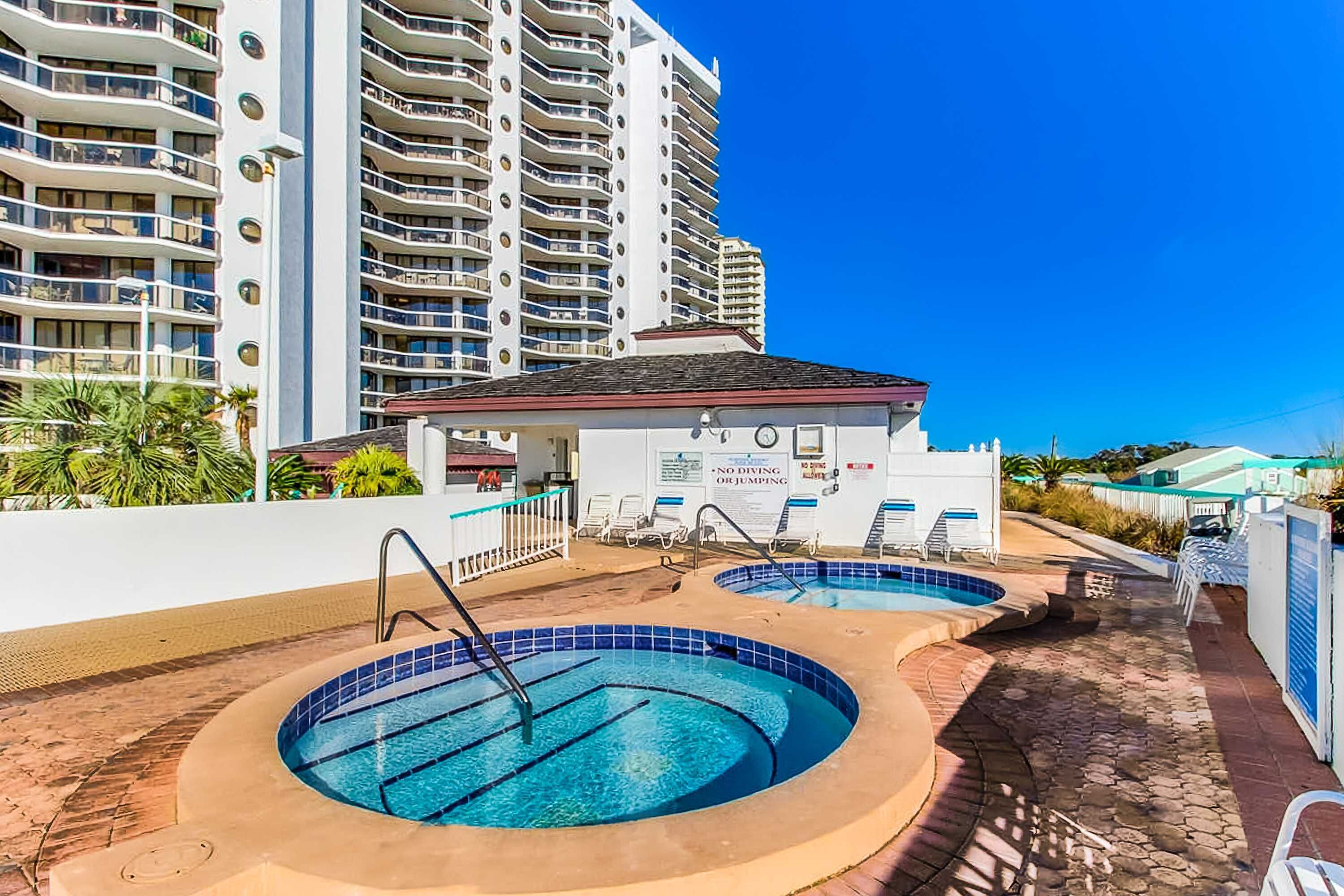 Un'area piscina con due piscine circolari, un piccolo edificio con un cartello e un hotel alto sullo sfondo.