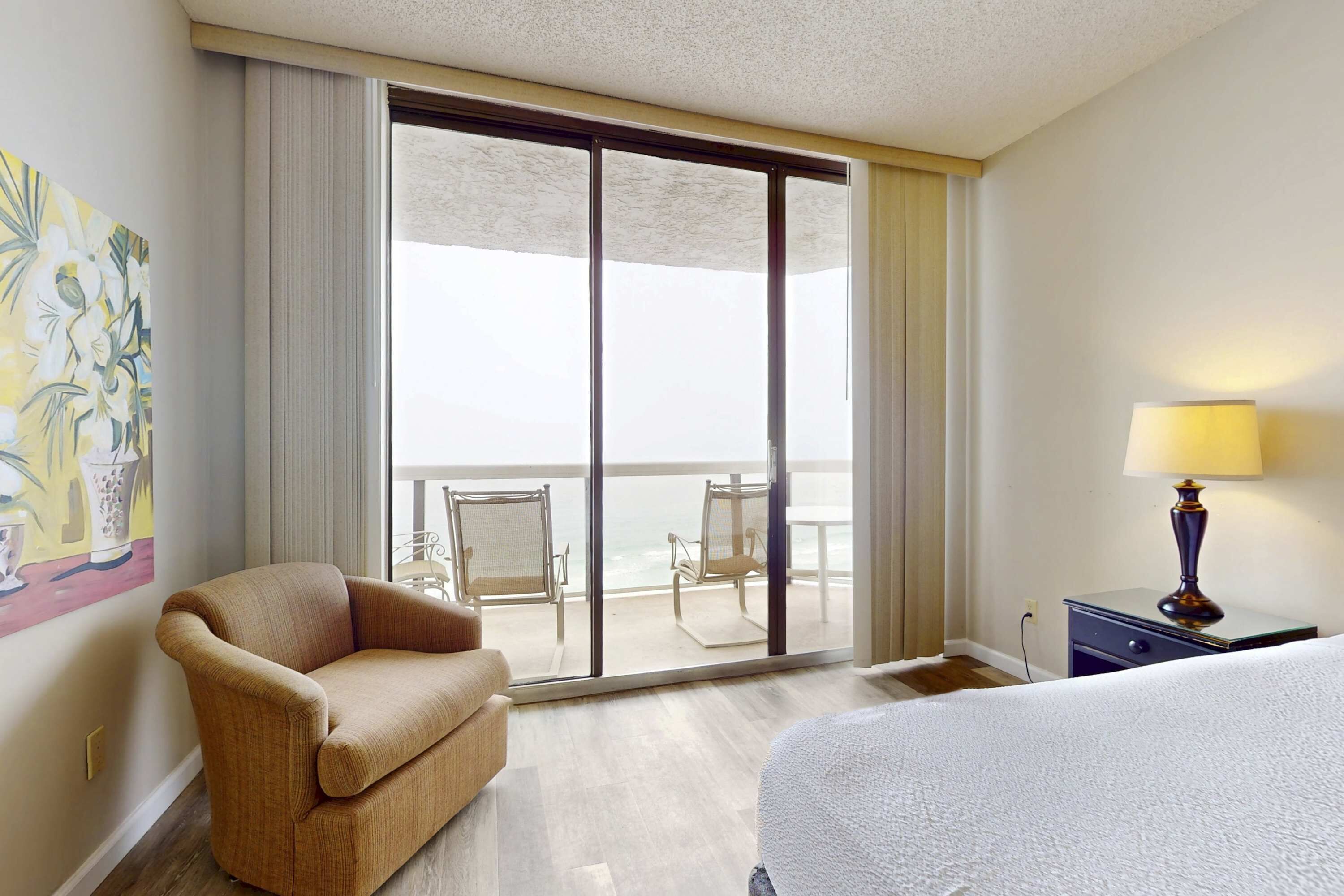 Una camera d'albergo con un letto, un divano, un balcone con sedie e un quadro appeso al muro.