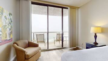 Una camera d'albergo con un letto, un divano, un balcone con sedie e un quadro appeso al muro.