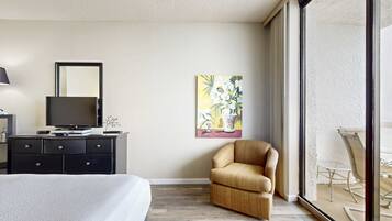 Una camera d'albergo con un letto, una televisione su un comò, una sedia, un quadro appeso al muro e un balcone con tavolo e sedie.
