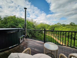 Eine Holzterrasse mit Whirlpool, Korbstühlen und einem Glastisch.