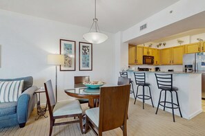 A modern kitchen with yellow cabinets, a central island with bar stools, and a dining area with a round table and chairs. - Coastal condo, shared pools, Onsite eateries, Spa, Wifi (Destin)