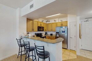 A kitchen with wooden cabinets, a granite countertop, a built-in microwave, a refrigerator, and a bar stool area. - Coastal condo, shared pools, Onsite eateries, Spa, Wifi (Destin)