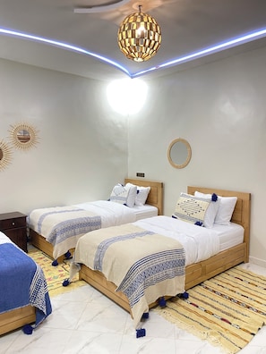 A bedroom with two beds, a ceiling light, and a wall-mounted mirror. - 

Amazigh Surf House- Cozy, Quiet, Wi-Fi, Equipped Kitchen . (Aourir, Marruecos)