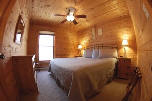 Un dormitorio de cabaña de madera acogedor, con cama, mesitas de noche, cómoda y ventilador de techo.