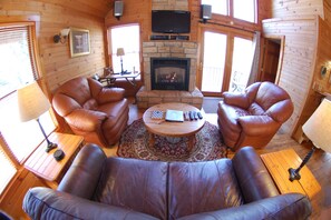 Una sala de estar acogedora con sofás de cuero, una chimenea, un televisor y un ventanal grande.
