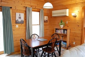 Una habitación con paneles de madera, una mesa de comedor, sillas, una estantería y una cama.
