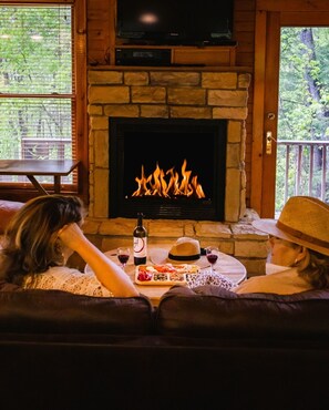 Una chimenea con detalles de piedra, un televisor encima y una mesa de comedor con comida y bebidas.