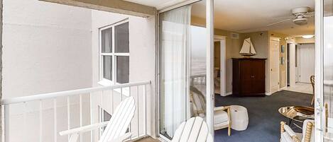 Un balcon avec des fauteuils Adirondack blancs, une porte-fenêtre coulissante donnant sur un salon doté d’une moquette bleue, d’une décoration sur le thème de la voile et d’un ventilateur de plafond.