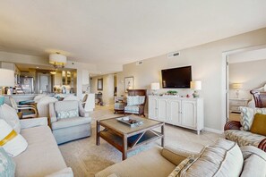Ein geräumiges Wohnzimmer mit einer großen Couch, einem Couchtisch und einem Fernseher. Im Hintergrund ist ein Essbereich mit Stühlen und einem Tisch zu sehen.