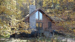 A cabin with a stone chimney, wooden exterior, and a large window. - Harvest Moon Cottages - Peacepipe   00088 (Rockbridge)
