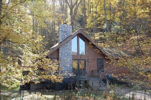 A cabin with a stone chimney, wooden exterior, and a large window. - Harvest Moon Cottages - Peacepipe   00088 (Rockbridge)