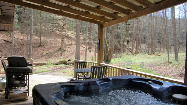 A hot tub area with a wooden deck, outdoor seating, and a view of a forested area. - Harvest Moon Cottages - Peacepipe   00088 (Rockbridge)