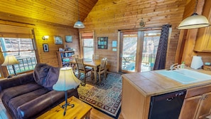 A cozy cabin interior with a wooden dining area, a sofa, a coffee table, and a kitchen with a sink and dishwasher. - Harvest Moon Cottages - Peacepipe   00088 (Rockbridge)