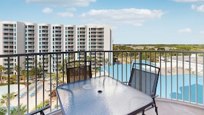 Un balcon avec une table et des chaises donnant sur une piscine et un grand bâtiment en arrière-plan.