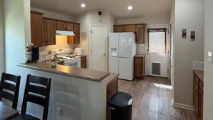 Cocina compacta con armarios de madera, un refrigerador blanco, estufa y un comedor con sillas.