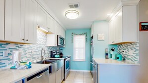 A kitchen with white cabinets, a microwave, a sink, and a dishwasher. - Gulf view condo with pool, balcony, full kitchen, nautical theme, W/D, & AC (Destin)
