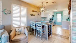 A modern kitchen with white cabinets, a dining area with a table and chairs, and decorative fish wall art. - Gulf view condo with pool, balcony, full kitchen, nautical theme, W/D, & AC (Destin)
