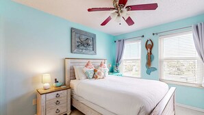 A bedroom with a bed, nightstand, and a ceiling fan. - Gulf view condo with pool, balcony, full kitchen, nautical theme, W/D, & AC (Destin)