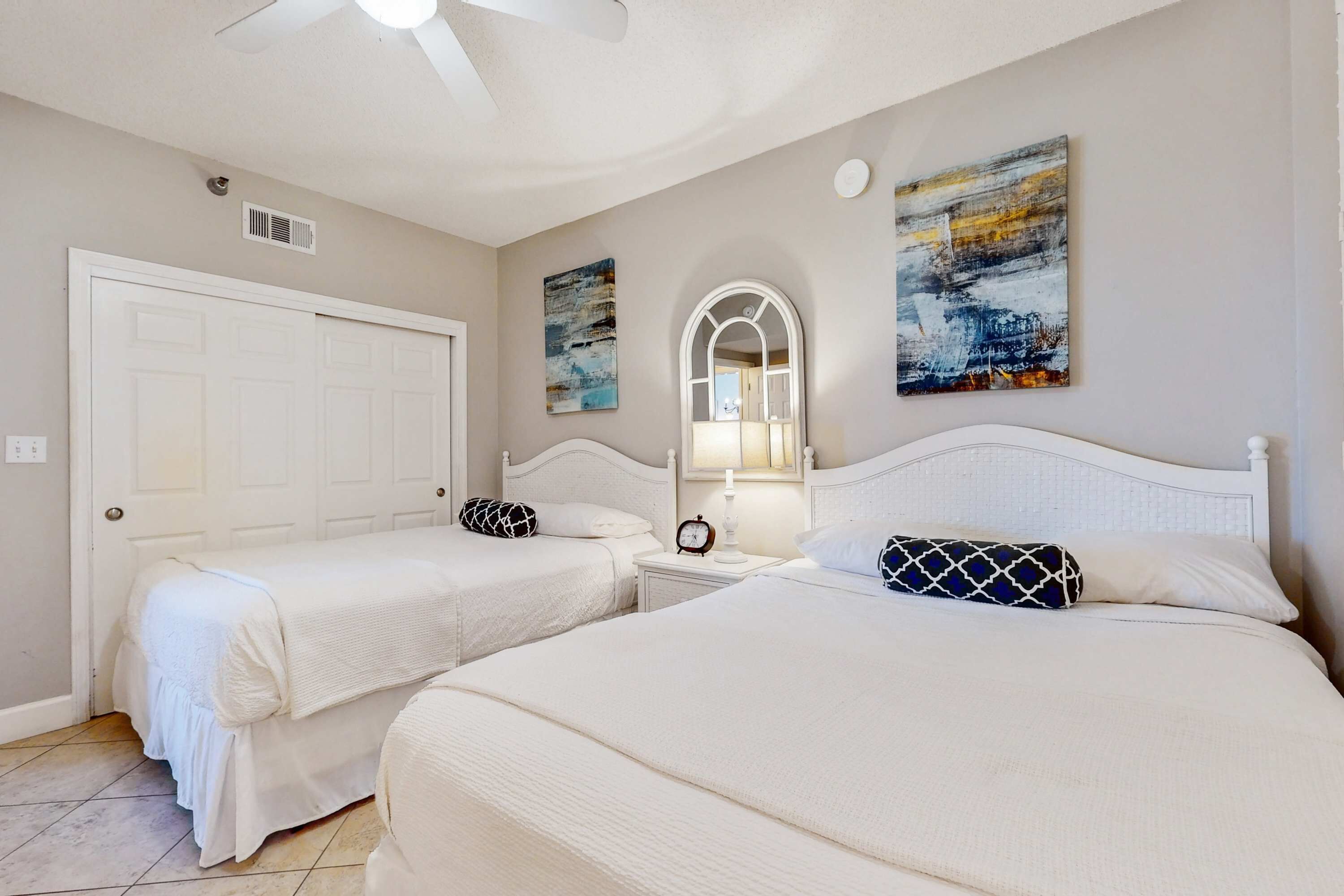 A bedroom with two beds, a ceiling fan, a door, and artwork on the walls.