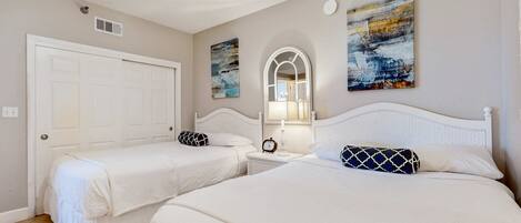A bedroom with two beds, a ceiling fan, a door, and artwork on the walls.