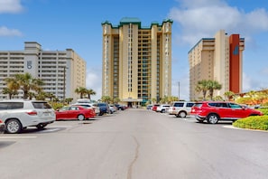 A parking lot with multiple cars, a tall hotel building with a green roof, and palm trees. - Gorgeous & cozy beachfront condo with pool & beach access (Destin)