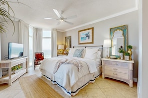 A hotel room with a bed, a TV, a desk, and a nightstand with a lamp. - Gorgeous & cozy beachfront condo with pool & beach access (Destin)