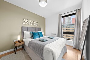 Une chambre moderne avec une tête de lit grise, du linge de lit blanc et un plaid à motifs gris.