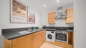 A modern kitchen with wooden cabinets, a built-in washing machine, and a stainless steel oven. - One bed apt opp tube station central line (London)