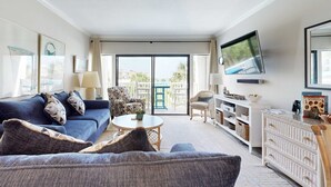 A modern living room with a blue sofa, a round coffee table, and a television mounted on the wall. - Snowbird-friendly condo with beach views, private beach, heated pool (Destin)