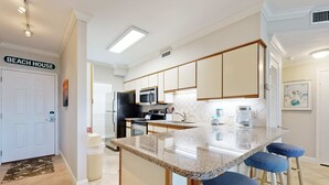 A modern kitchen with a central island, bar stools, and a microwave. - Snowbird-friendly condo with beach views, private beach, heated pool (Destin)