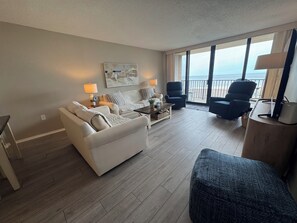 A living room with a sofa, armchairs, a coffee table, and a view of the ocean through large windows.