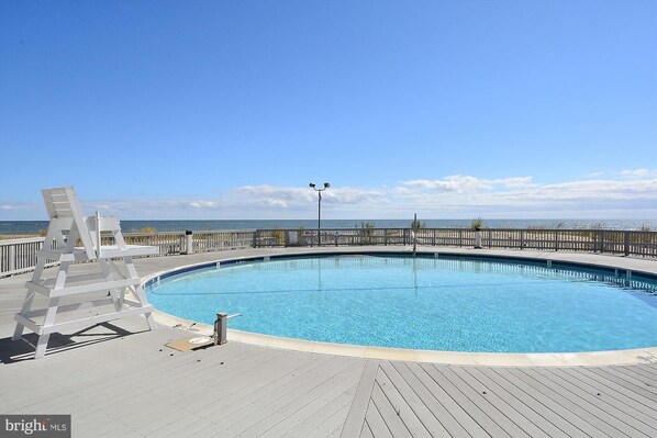 A circular pool with a wooden deck, a white chair, and a view of the ocean.
