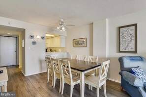 A dining area with a wooden table and white chairs, a ceiling fan, and a framed map on the wall.