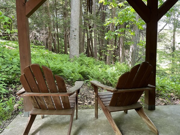 Dos sillas Adirondack de madera bajo una pérgola de madera en un área boscosa.