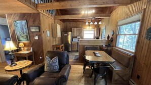 A cozy cabin interior with a dining area, kitchen, and seating space. - Creeksong-Harvest Moon (Logan)