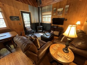 Interior acogedor de una cabaña con chimenea, mobiliario de cuero, televisión y obras de arte en las paredes.