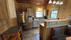 A wooden cabin-style kitchen with a refrigerator, microwave, sink, and wooden cabinets. - Creeksong-Harvest Moon (Logan)